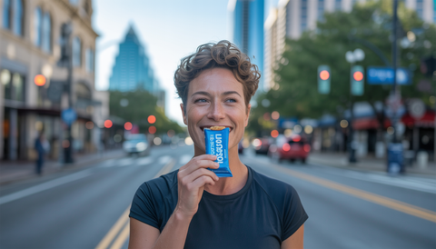 Person eating a low sugar protein bar on an Austin street, with city landmarks in the background.